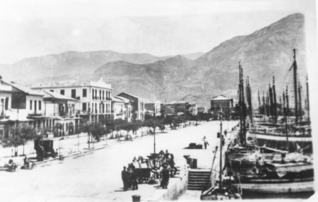 Το λιμάνι γεμάτο καϊκια που εκτελούσαν συγκοινωνιακό έργο ελλείψει δρόμων, η άμαξα που περιμένεις επιβάτες, το "Αμέρικα" αριστερά και το "Πανελλήνιον" στο βάθος